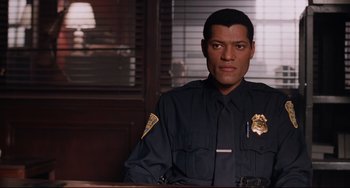 Movie still from “Deep Cover” (1992), directed by Bill Duke – A police officer sitting at a table in a room; Medium shot, Over the shoulder angle