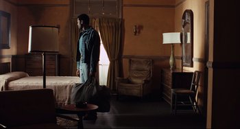 Movie still from “Deep Cover” (1992), directed by Bill Duke – A man standing next to a bed in a room; Wide shot, High angle
