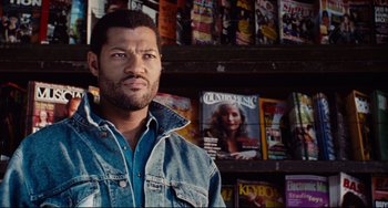 Movie still from “Deep Cover” (1992), directed by Bill Duke – A man standing in front of a shelf of magazines; Close Up shot, Over the shoulder angle