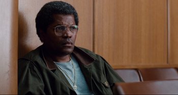 Movie still from “Deep Cover” (1992), directed by Bill Duke – A man in a green jacket sitting in front of a wooden wall; Close Up shot, Over the shoulder angle