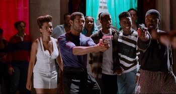 Movie still from “Deep Cover” (1992), directed by Bill Duke – A group of men and women standing around a man holding a cell phone in his hand; Medium shot, Low angle