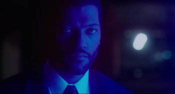 Movie still from “Deep Cover” (1992), directed by Bill Duke – A person wearing a suit and tie; Close Up shot, Over the shoulder angle