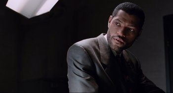 Movie still from “Deep Cover” (1992), directed by Bill Duke – A man wearing a suit and tie in a dark room; Close Up shot, Over the shoulder angle