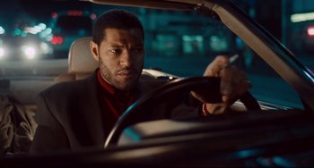 Movie still from “Deep Cover” (1992), directed by Bill Duke – A man in a suit driving a car at night; Close Up shot, Over the shoulder angle