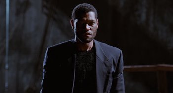 Movie still from “Deep Cover” (1992), directed by Bill Duke – A man wearing a suit and a black sweater; Close Up shot, Low angle