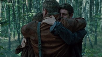 Movie still from “Defiance” (2008), directed by Edward Zwick – A group of men hugging each other in the woods; Medium shot, Over the shoulder angle