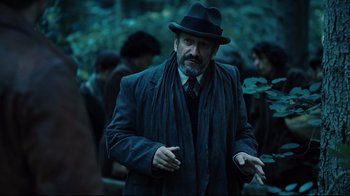 Movie still from “Defiance” (2008), directed by Edward Zwick – A man wearing a hat and a coat; Medium shot, Over the shoulder angle