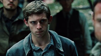 Movie still from “Defiance” (2008), directed by Edward Zwick – A young man with short blonde hair wearing a blue shirt; Close Up shot, Over the shoulder angle