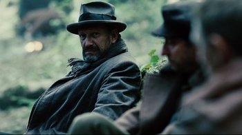 Movie still from “Defiance” (2008), directed by Edward Zwick – A man wearing a hat and a coat sitting next to another man wearing a hat; Close Up shot, Over the shoulder angle