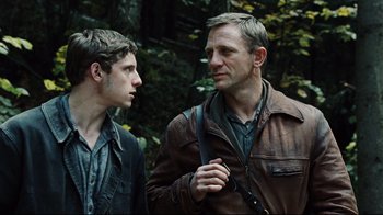 Movie still from “Defiance” (2008), directed by Edward Zwick – Two men standing next to each other in the woods; Close Up shot, Over the shoulder angle