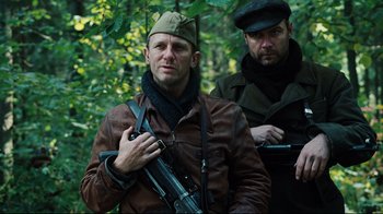 Movie still from “Defiance” (2008), directed by Edward Zwick – Two men in the woods holding guns and posing for a picture; Medium shot, Low angle