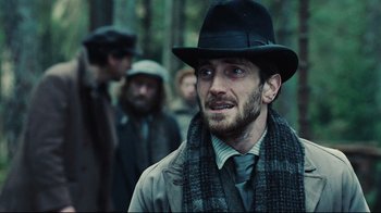 Movie still from “Defiance” (2008), directed by Edward Zwick – A man in a hat and a scarf standing in front of a group of men; Close Up shot, Over the shoulder angle