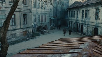 Movie still from “Defiance” (2008), directed by Edward Zwick – Two people are walking down the street in the middle of the day; Extreme Wide shot, High angle