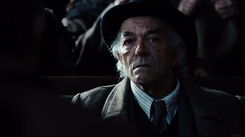 Movie still from “Defiance” (2008), directed by Edward Zwick – An old man wearing a hat sitting in a chair; Close Up shot, Over the shoulder angle