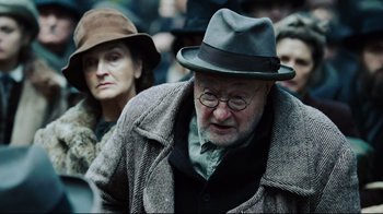 Movie still from “Defiance” (2008), directed by Edward Zwick – An old man wearing a hat and glasses; Close Up shot, Over the shoulder angle