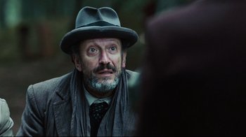 Movie still from “Defiance” (2008), directed by Edward Zwick – An old man with a beard wearing a hat and a tie; Close Up shot, Over the shoulder angle