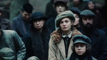 Movie still from “Defiance” (2008), directed by Edward Zwick – A group of people standing around each other wearing hats and coats; Medium shot, Over the shoulder angle