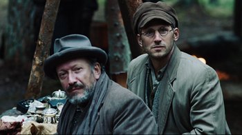 Movie still from “Defiance” (2008), directed by Edward Zwick – Two men in hats and jackets standing next to each other; Medium shot, Low angle