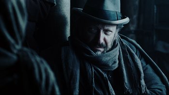 Movie still from “Defiance” (2008), directed by Edward Zwick – A man wearing a hat and a scarf looking at the camera; Close Up shot, Over the shoulder angle