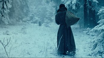 Movie still from “Defiance” (2008), directed by Edward Zwick – A person walking in the snow holding a bag; Wide shot, Over the shoulder angle