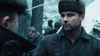 Movie still from “Defiance” (2008), directed by Edward Zwick – A man wearing a russian hat in the woods; Close Up shot, Over the shoulder angle