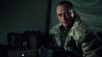 Movie still from “Defiance” (2008), directed by Edward Zwick – A man in a fur lined jacket and a bottle; Close Up shot, Over the shoulder angle