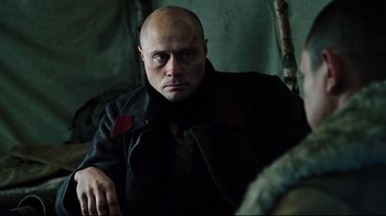 Movie still from “Defiance” (2008), directed by Edward Zwick – A bald man in a black coat is looking at the camera; Close Up shot, Over the shoulder angle