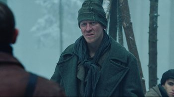Movie still from “Defiance” (2008), directed by Edward Zwick – A man wearing a green coat and a green hat; Medium shot, Low angle