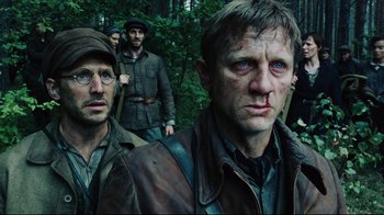 Movie still from “Defiance” (2008), directed by Edward Zwick – A group of men standing next to each other in the woods; Close Up shot, Over the shoulder angle