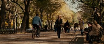 Movie still from “Definitely, Maybe” (2008), directed by Adam Brooks – A woman walking down a sidewalk near a park with a bicycle; Wide shot, Over the shoulder angle