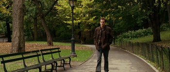 Movie still from “Definitely, Maybe” (2008), directed by Adam Brooks – A man standing on a sidewalk next to a park bench; Wide shot, Over the shoulder angle