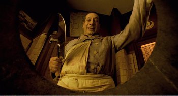 Movie still from “Delicatessen” (1991), directed by Marc Caro – A man holding a large spatula in a room; Medium shot, Overhead angle
