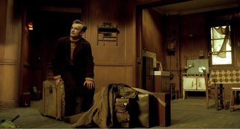 Movie still from “Delicatessen” (1991), directed by Marc Caro – A man standing in front of a pile of luggage; Wide shot, High angle