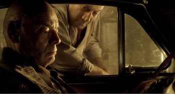 Movie still from “Delicatessen” (1991), directed by Marc Caro – A man sitting in the back seat of a car while another man looks on; Medium shot, Low angle