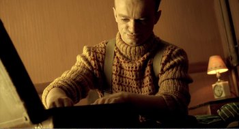 Movie still from “Delicatessen” (1991), directed by Marc Caro – A man wearing a sweater and suspenders is playing a piano; Medium shot, Low angle