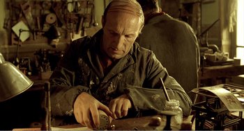 Movie still from “Delicatessen” (1991), directed by Marc Caro – An old man is working on something on a table; Close Up shot, Low angle