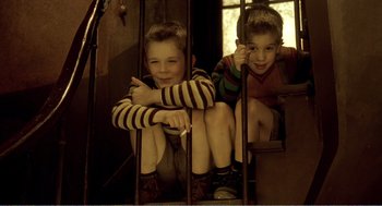 Movie still from “Delicatessen” (1991), directed by Marc Caro – Two young boys sitting in a cage looking at the camera; Medium shot, High angle