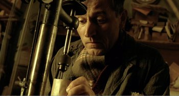 Movie still from “Delicatessen” (1991), directed by Marc Caro – A man looking through a microscope at a piece of paper; Close Up shot, High angle