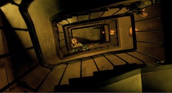 Movie still from “Delicatessen” (1991), directed by Marc Caro – A woman sitting on top of a spiral stair case; Extreme Wide shot, Overhead angle