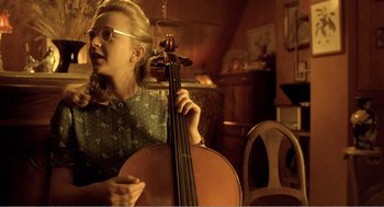 Movie still from “Delicatessen” (1991), directed by Marc Caro – A woman is holding a cello in a room; Medium shot, Over the shoulder angle