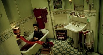 Movie still from “Delicatessen” (1991), directed by Marc Caro – A man sitting in a bath tub in a bathroom; Wide shot, Overhead angle