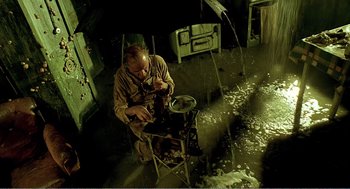 Movie still from “Delicatessen” (1991), directed by Marc Caro – A man sitting on a chair in a room; Wide shot, High angle