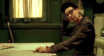 Movie still from “Delicatessen” (1991), directed by Marc Caro – A woman sitting at a table in front of a window; Close Up shot, Low angle