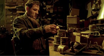 Movie still from “Delicatessen” (1991), directed by Marc Caro – A man sitting in front of a table filled with boxes; Medium shot, Low angle