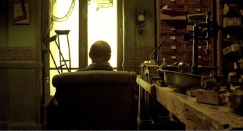 Movie still from “Delicatessen” (1991), directed by Marc Caro – A man sitting in a chair in front of a window; Wide shot, Low angle