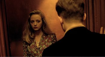 Movie still from “Delicatessen” (1991), directed by Marc Caro – A woman looking in the mirror while standing next to a man in a suit; Medium shot, Over the shoulder angle