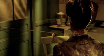 Movie still from “Delicatessen” (1991), directed by Marc Caro – A woman is holding a stick in a room; Medium shot, Over the shoulder angle