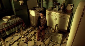 Movie still from “Delicatessen” (1991), directed by Marc Caro – A woman sitting on the floor of a kitchen next to an oven; Wide shot, Overhead angle