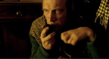 Movie still from “Delicatessen” (1991), directed by Marc Caro – A man in a green sweater is holding something in his mouth; Close Up shot, High angle