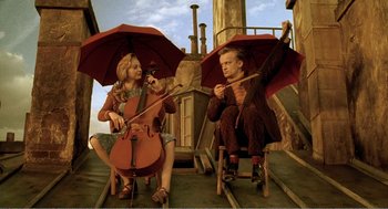 Movie still from “Delicatessen” (1991), directed by Marc Caro – A man and a woman sitting on chairs holding umbrellas; Medium shot, Low angle